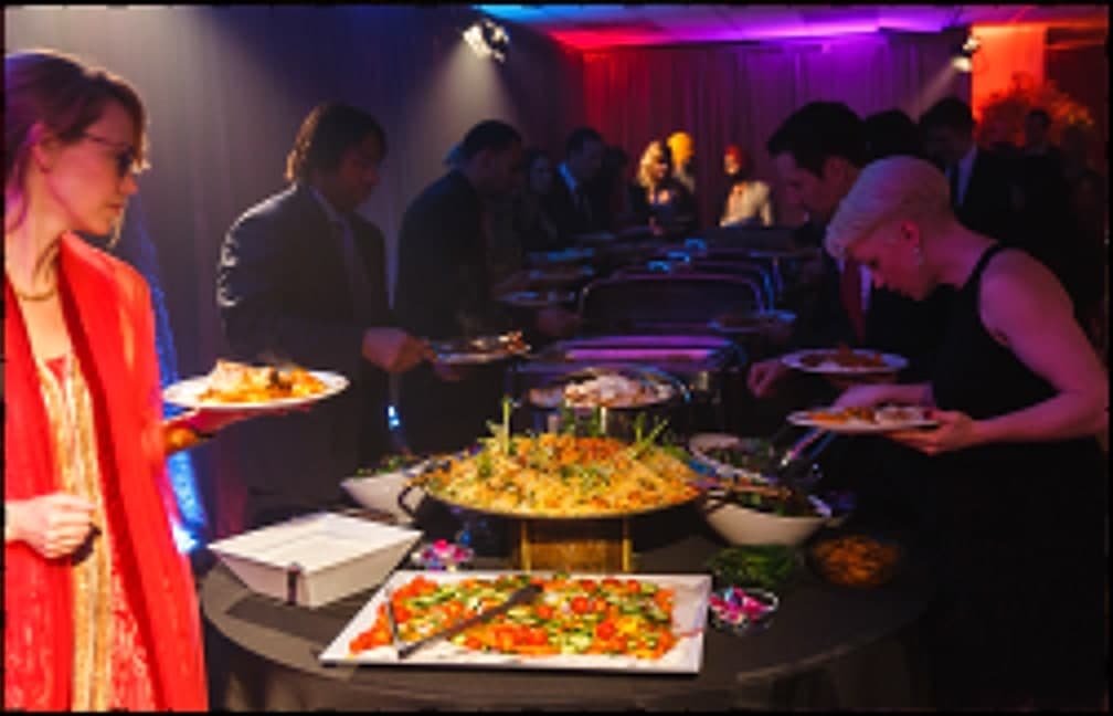 Wedding guests serving themselves at a Jewel of India catered buffet under stage lighting