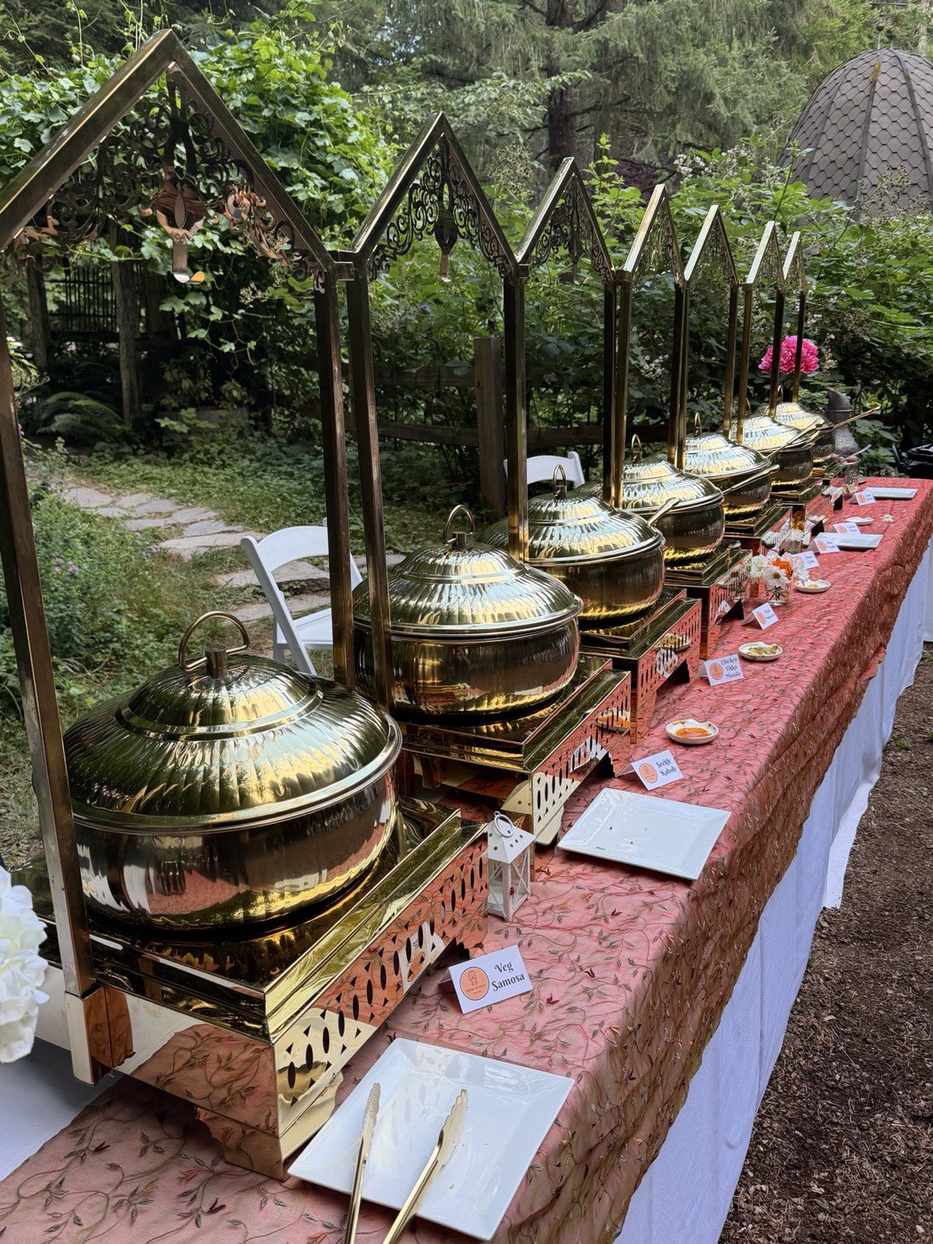 Brass chafing dishes under ornate arches on a blush embroidered table at an outdoor Indian wedding reception in Seattle